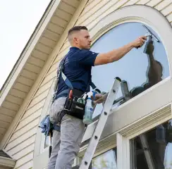 Professional window cleaner on a ladder using a squeegee to clean an exterior arched window, Fresno, CA.